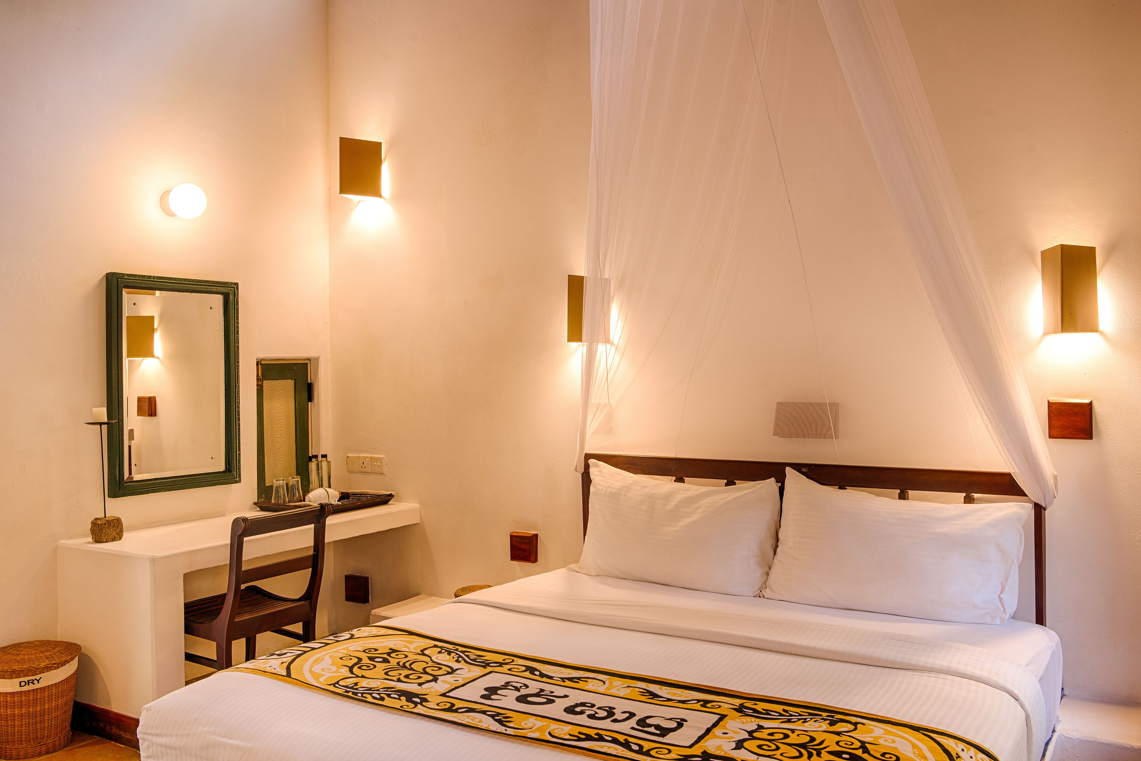 A neatly made bed with a canopy, a bedside table with a mirror, and wall-mounted lights.
