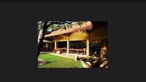 An outdoor dining area with tables and chairs, surrounded by a well-maintained lawn and a large tree. - Jetwing Ayurveda Pavilions (Negombo)