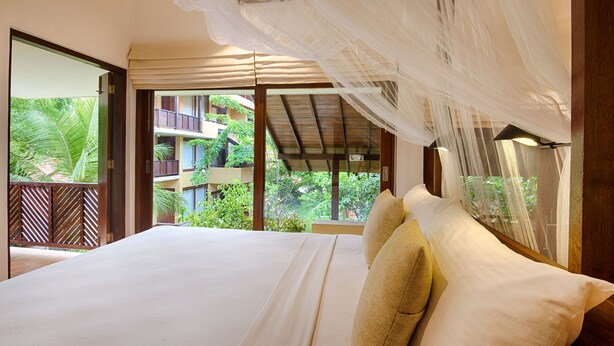 A bedroom with a large bed, a view of a balcony, and a mosquito net. - Jetwing Ayurveda Pavilions (Negombo)