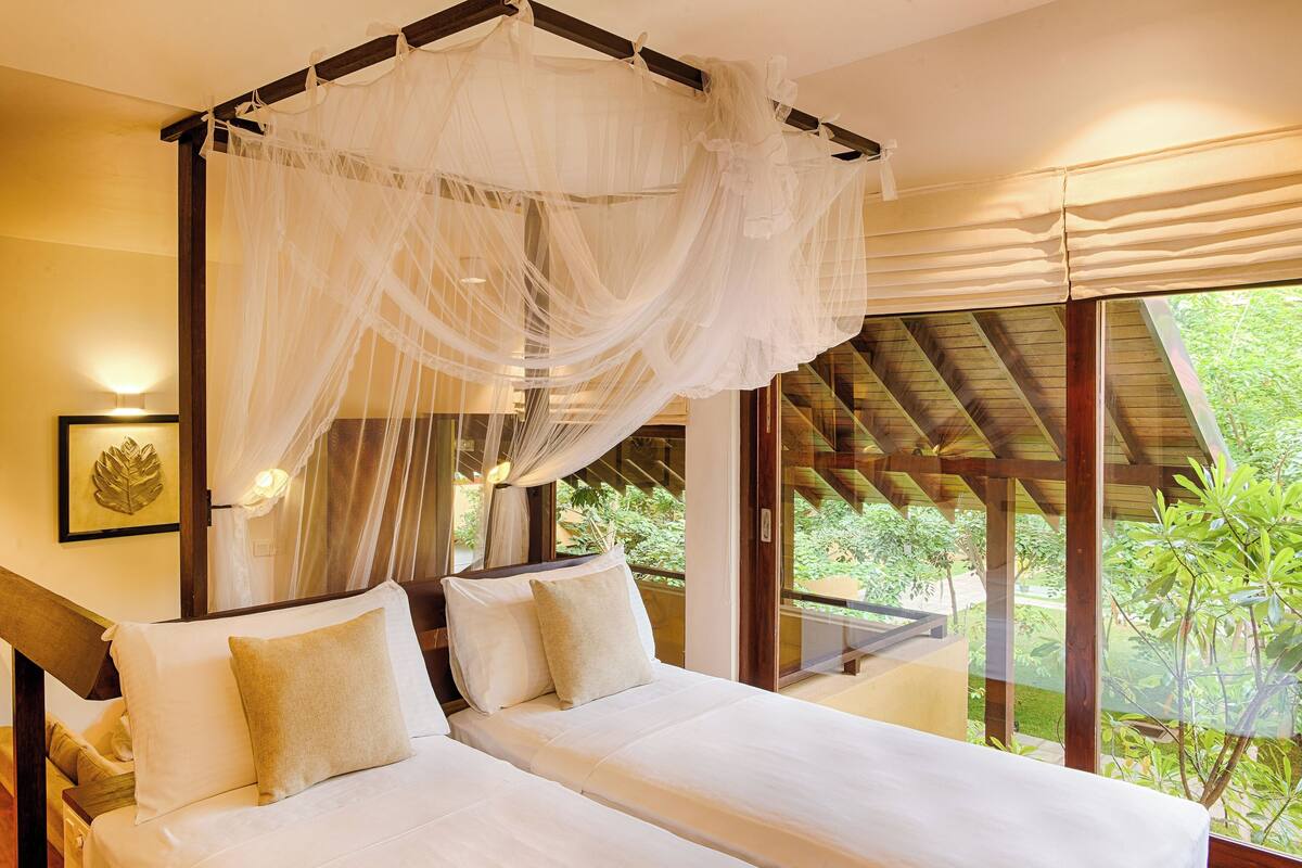A bedroom with a canopy bed, a view of greenery outside, and a framed leaf artwork on the wall.