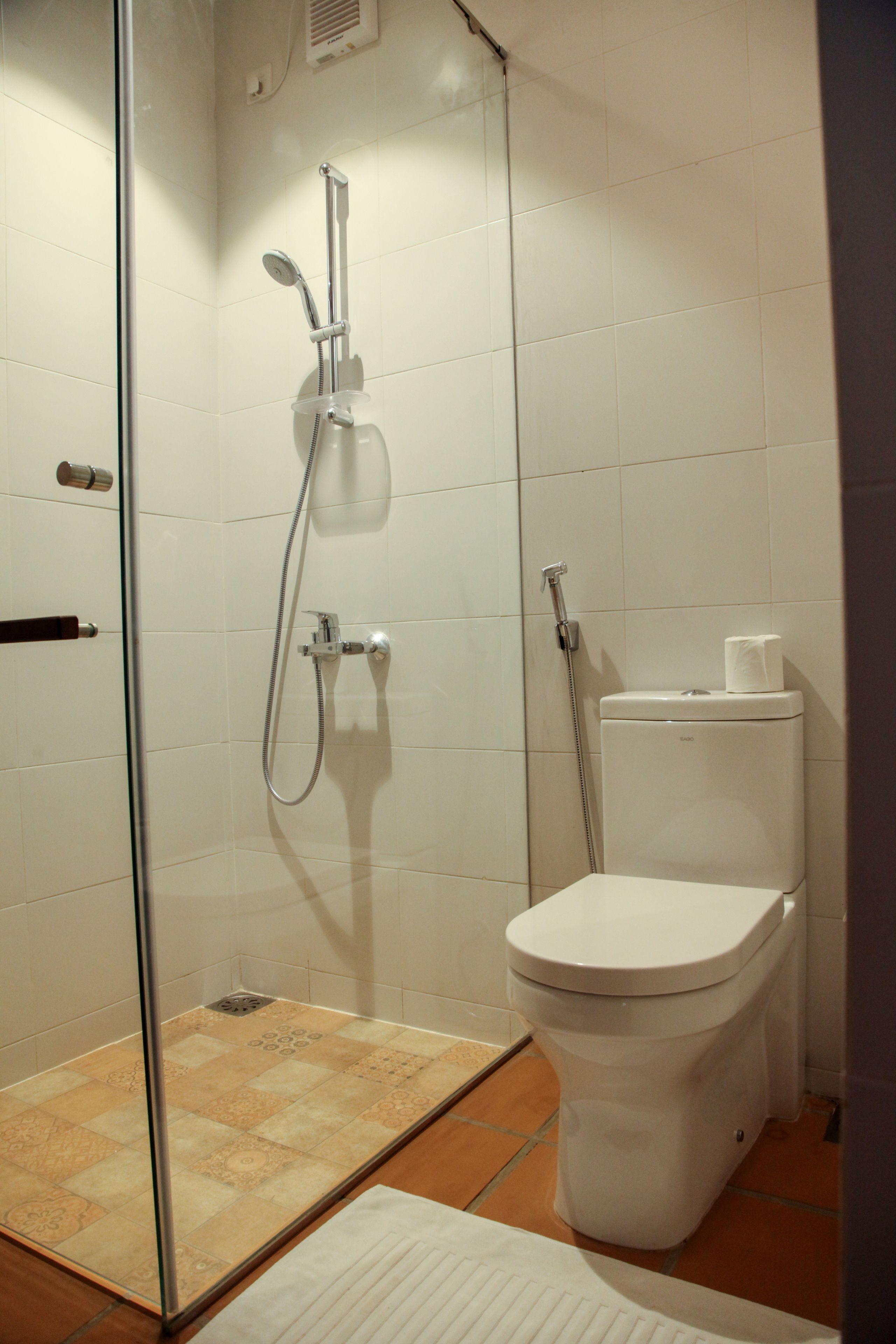 Une salle de bain avec une douche à parois de verre, des toilettes blanches et un sol carrelé.