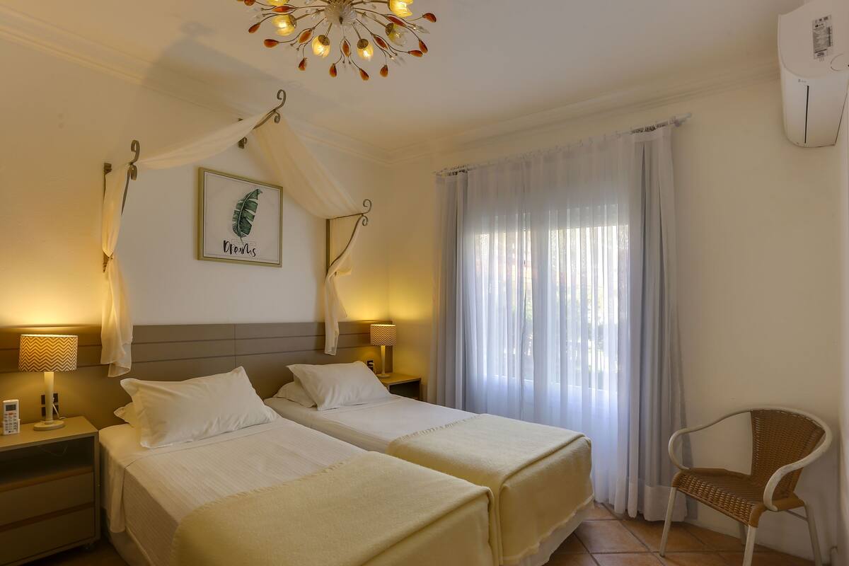 Ein Hotelzimmer mit zwei Betten, einem Himmelbett, einem Korbsessel und einer wandmontierten Klimaanlage.