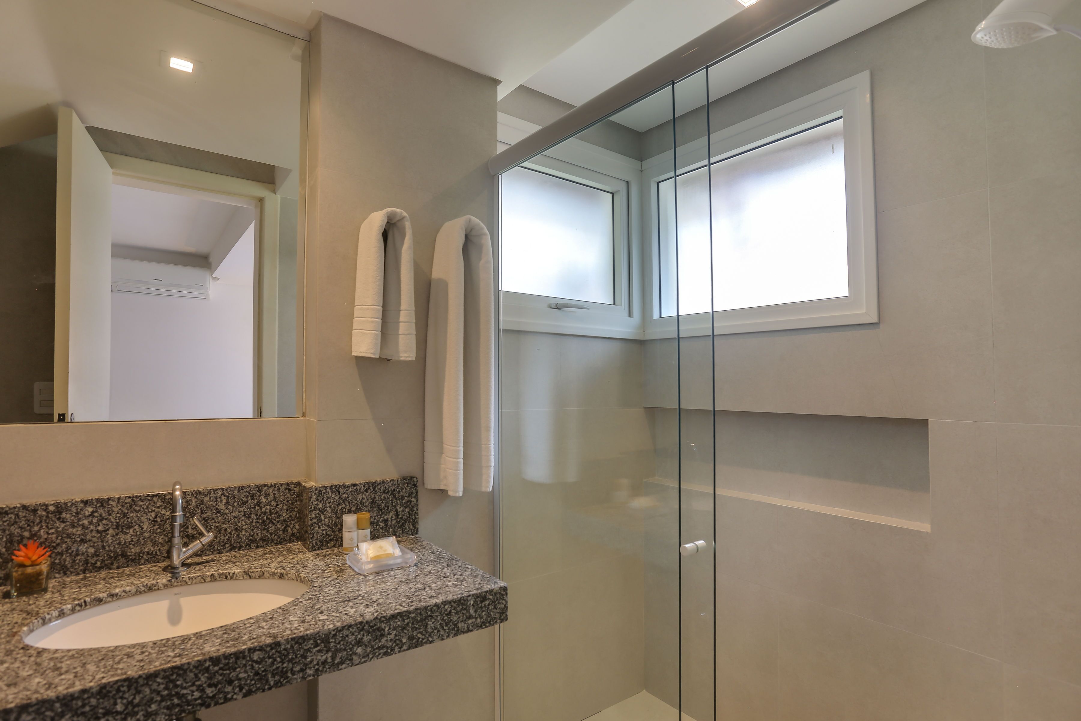 A modern bathroom with a granite countertop sink, a glass shower enclosure, and a large mirror.
