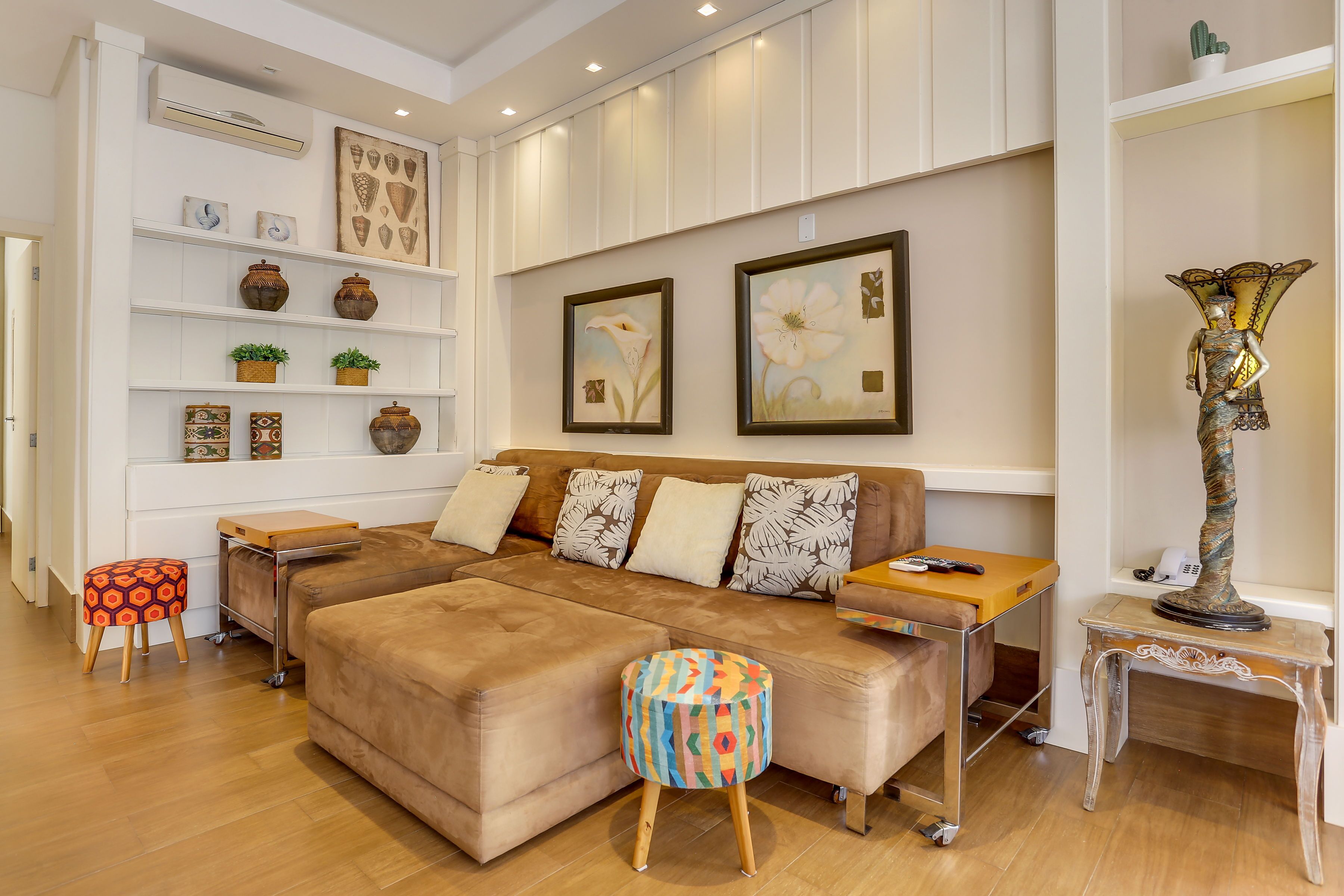 A modern living room with a brown sectional sofa, a colorful ottoman, a small wooden side table, and a decorative floor lamp.