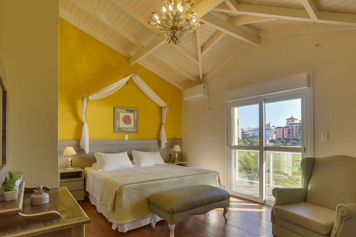 Ein Schlafzimmer mit Himmelbett, einer Sitzecke mit Sessel, einem Holztisch und einem großen Fenster mit Blick auf Gebäude.