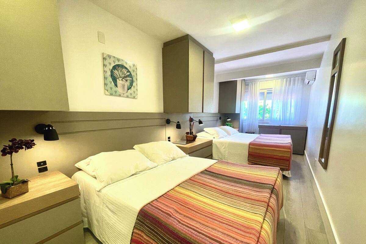 Ein Hotelzimmer mit zwei Betten, einem Nachttisch mit Lampe, einer Wanduhr und einem Fenster mit Vorhängen.