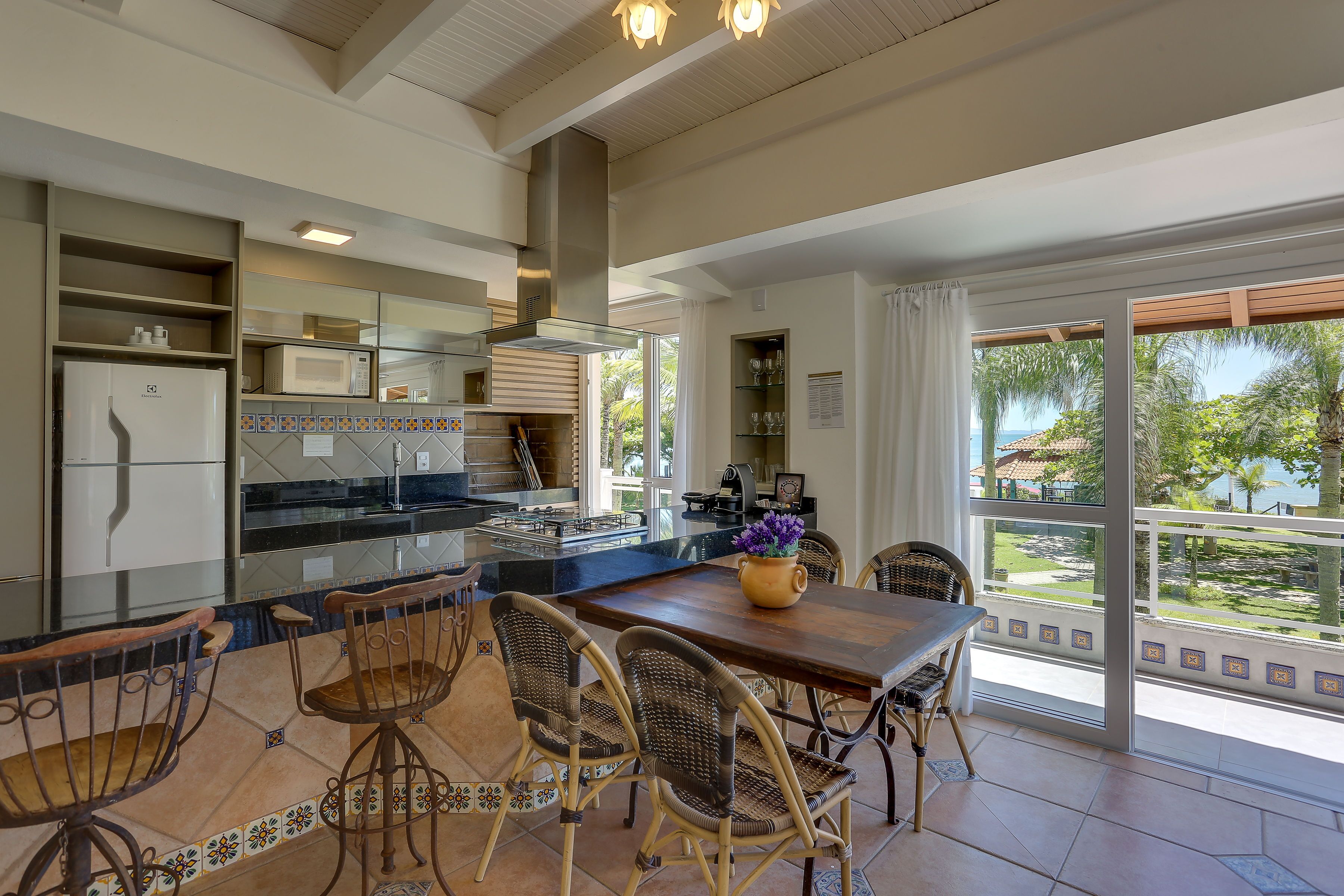A modern kitchen with a dining area, large windows, and a view of the outdoors.