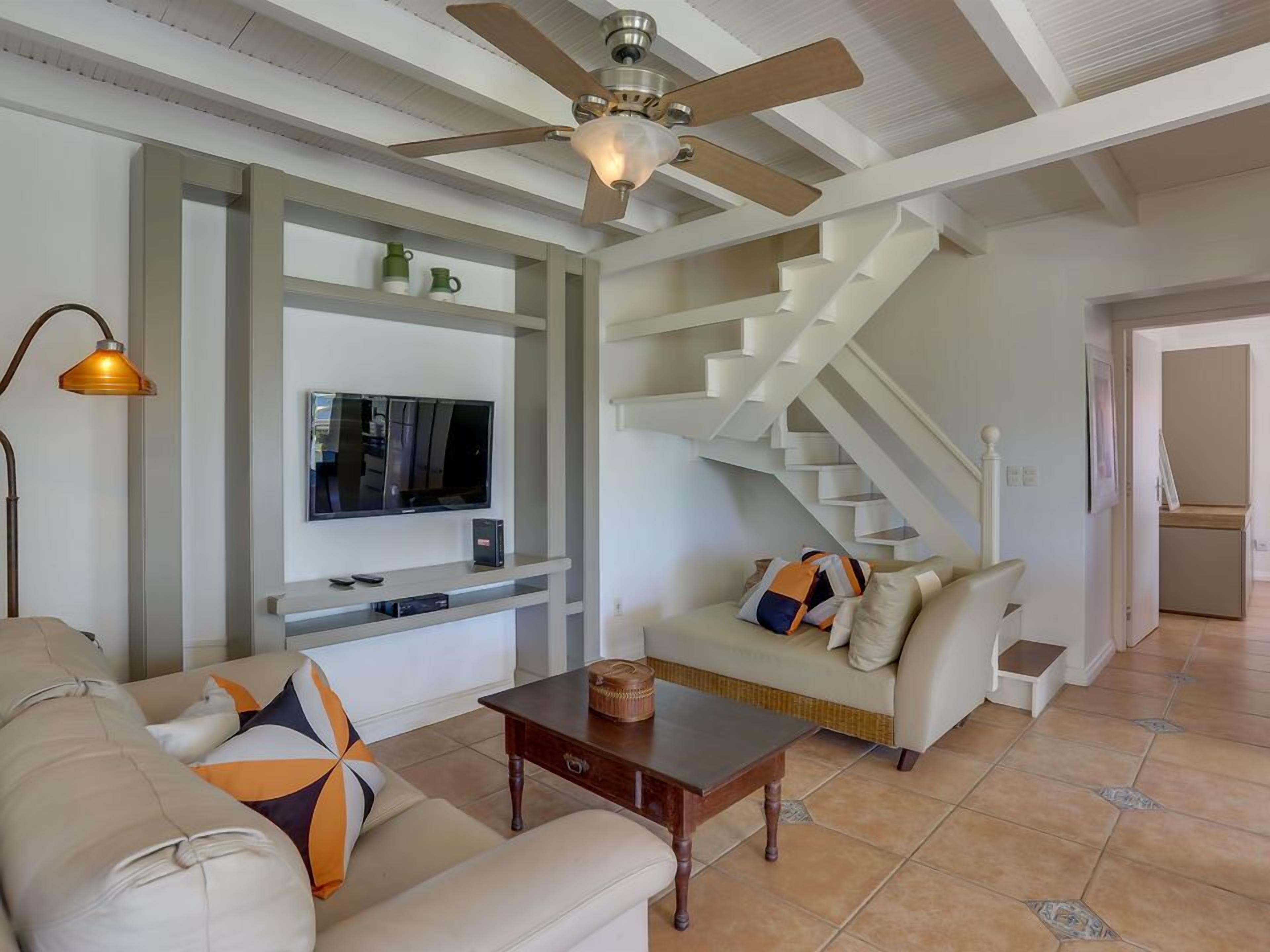 Una sala de estar con sofá, mesa de centro, televisor y una escalera.