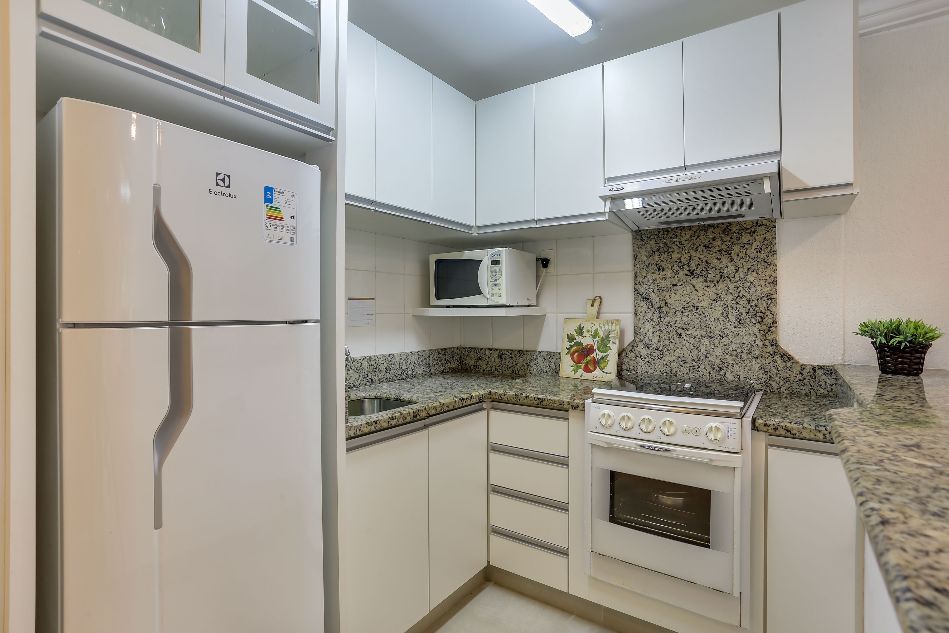 Una cocina compacta con armarios blancos, un microondas integrado, una estufa y un refrigerador.