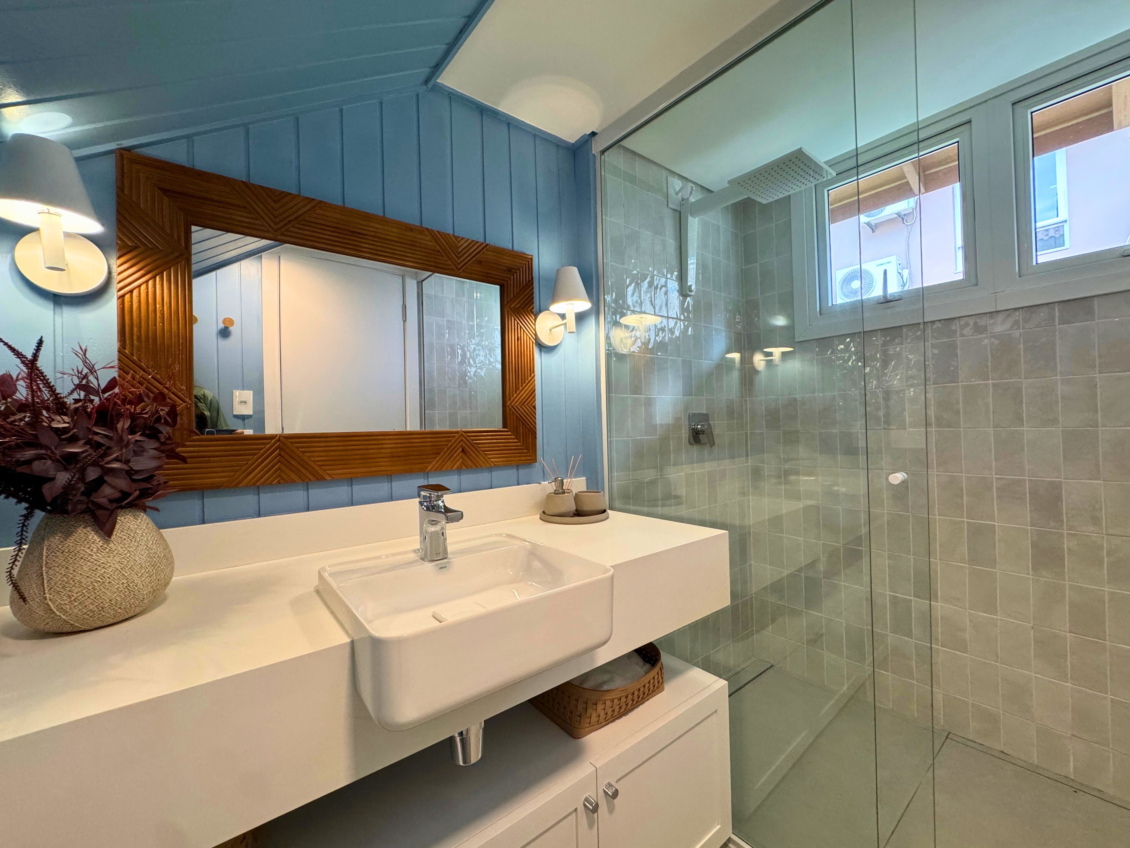 Ein Badezimmer mit einem weißen Waschbecken, einem spiegel mit Holzrahmen und einer Duschkabine aus Glas.