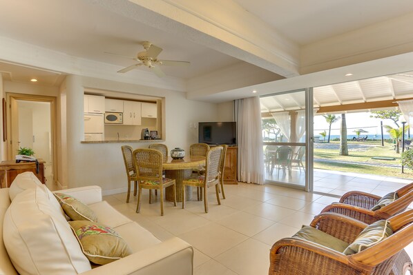 A spacious living area with a dining table, wicker chairs, a sofa, and a TV.
