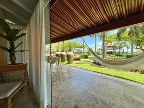 A covered patio area with a hammock, a seating area with a chair and table, and a view of a well-maintained garden and buildings in the distance.