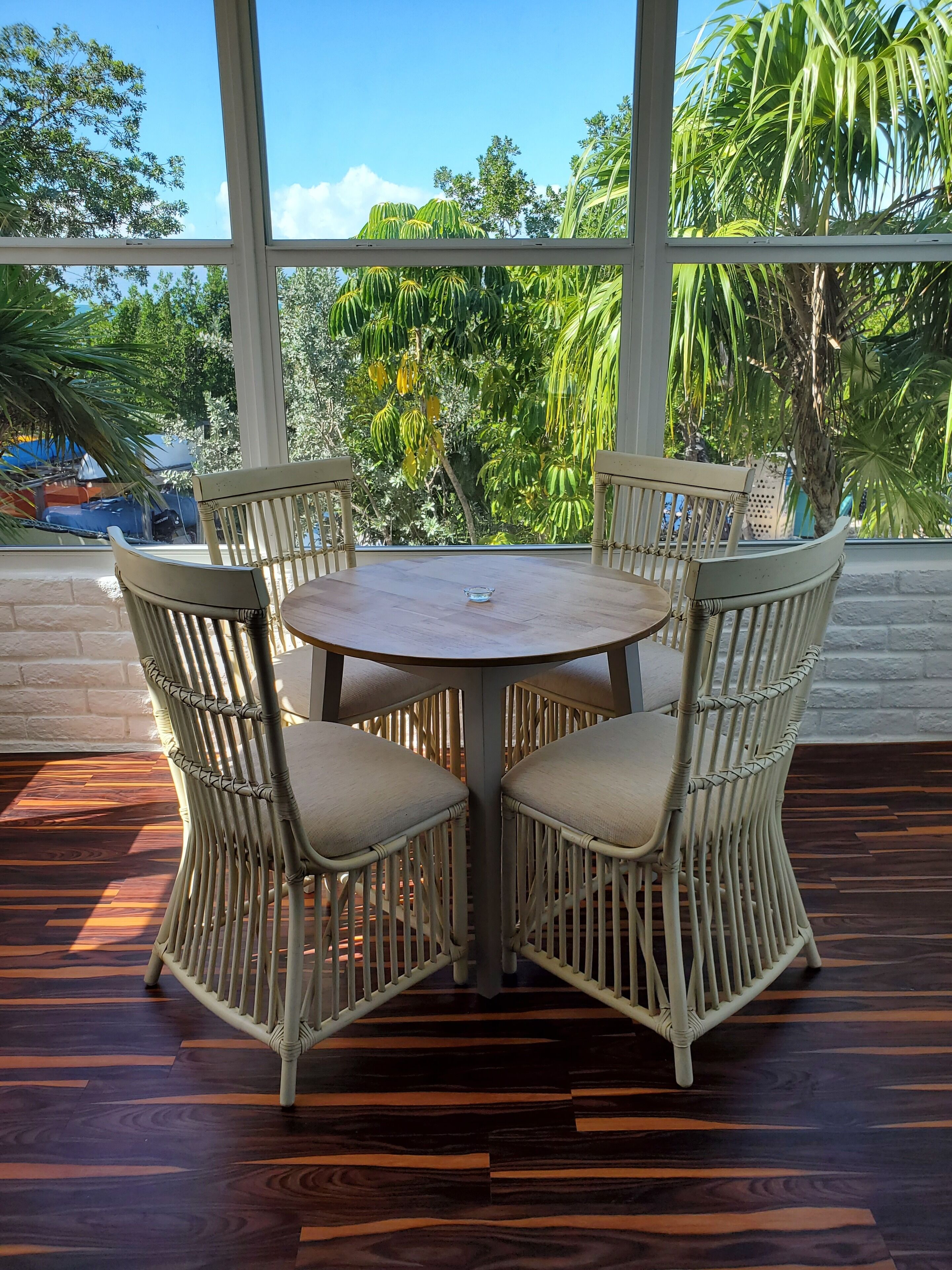 A round table with four wicker chairs, surrounded by a wooden floor with a herringbone pattern.