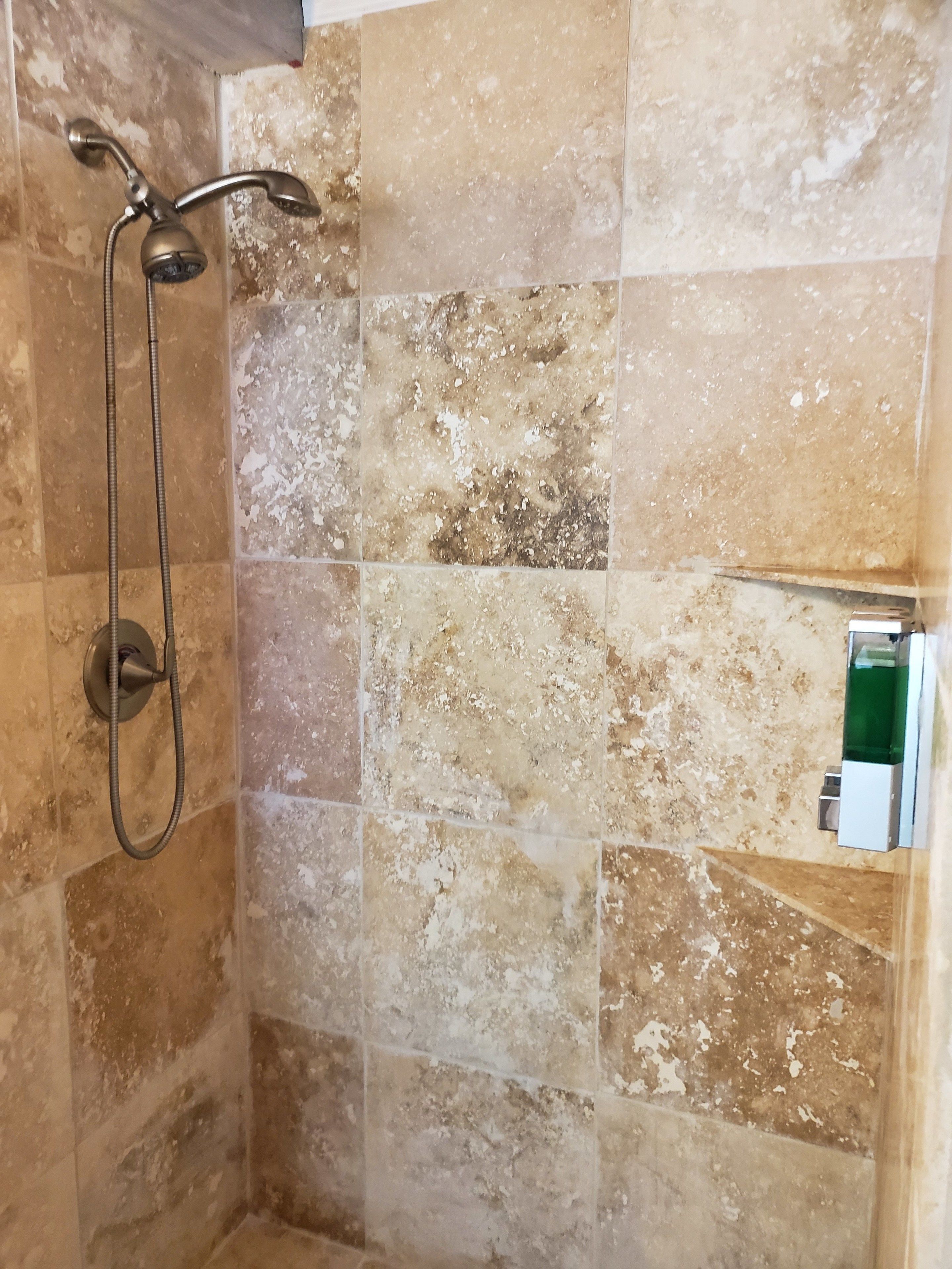 A shower area with a handheld showerhead and a fixed showerhead, tiled walls, and a small shelf with a bottle.