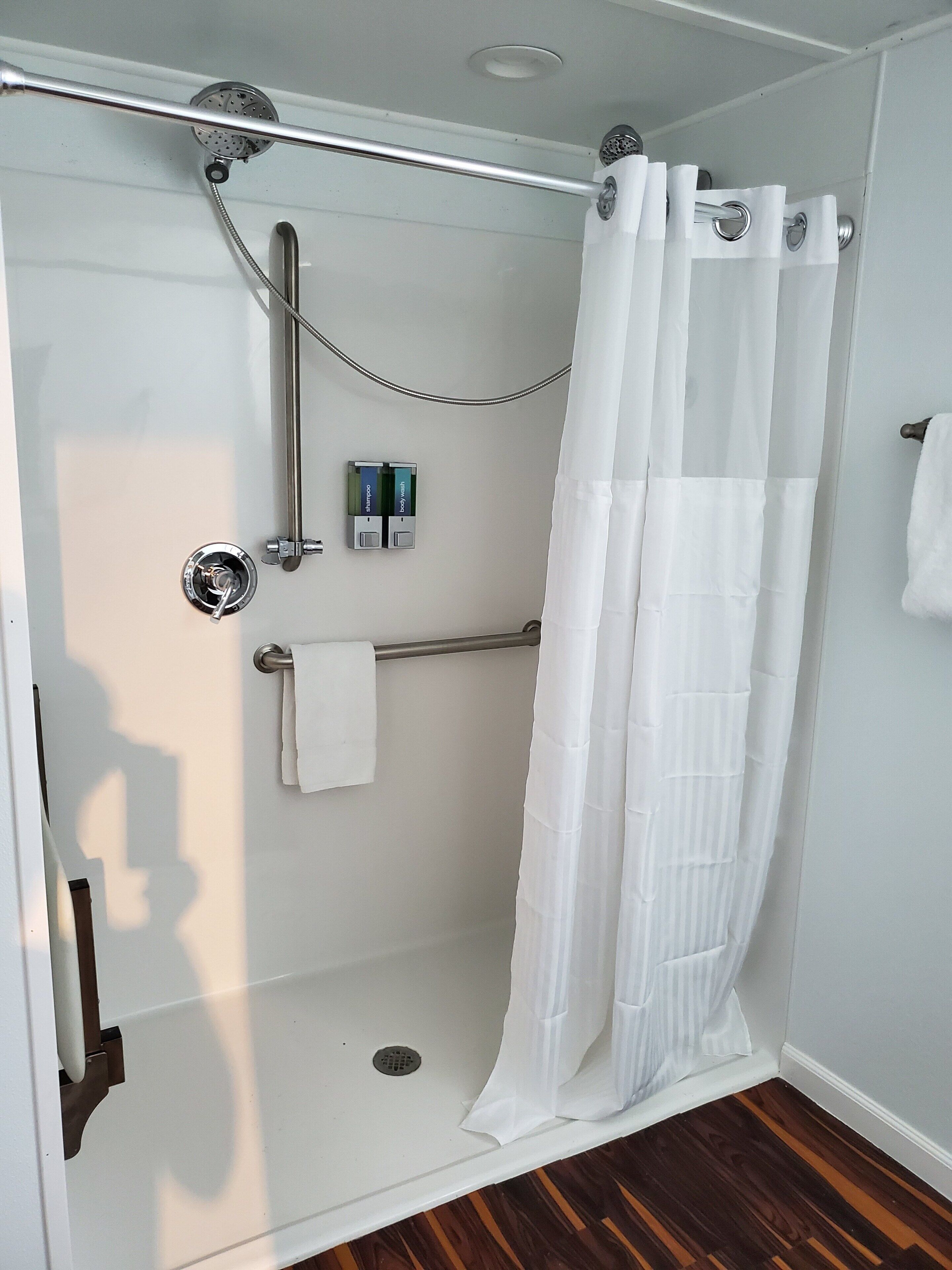 A walk-in shower with a glass door, a showerhead, a handheld shower, a towel rack, and a shower caddy with toiletries.