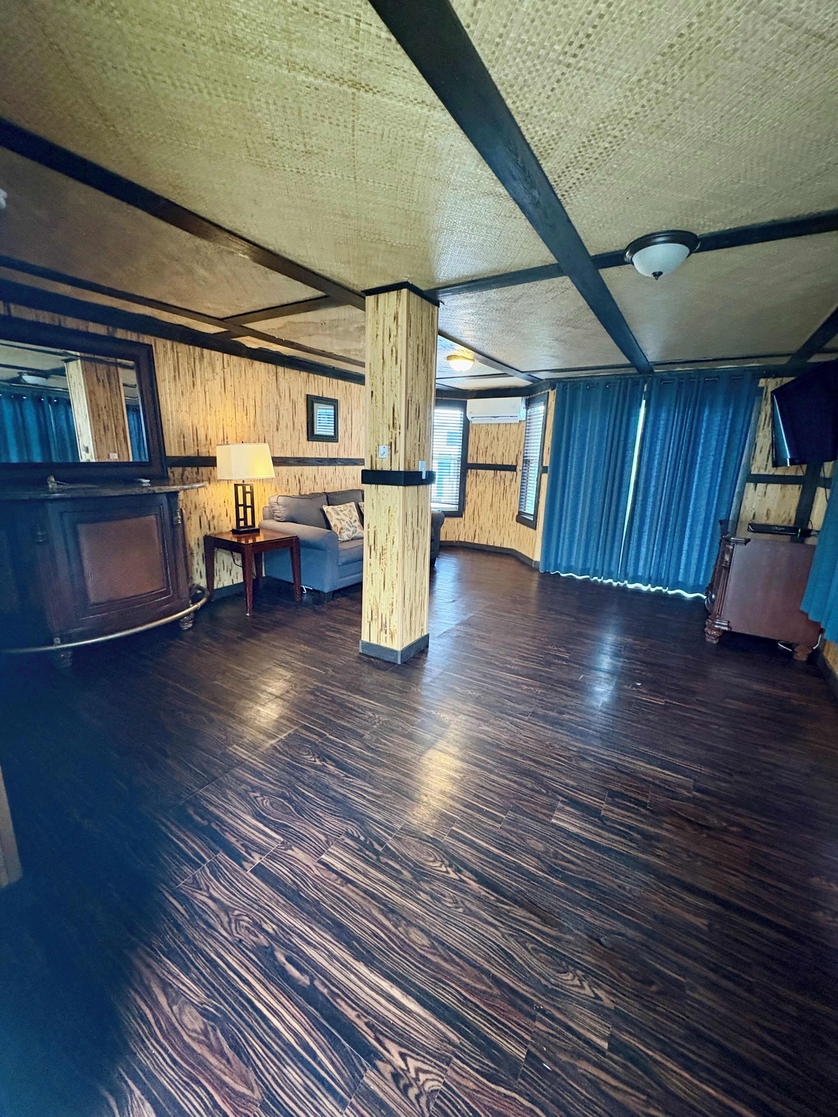 Um quarto espaçoso com piso de madeira, um pilar grande, um sofá e uma televisão.