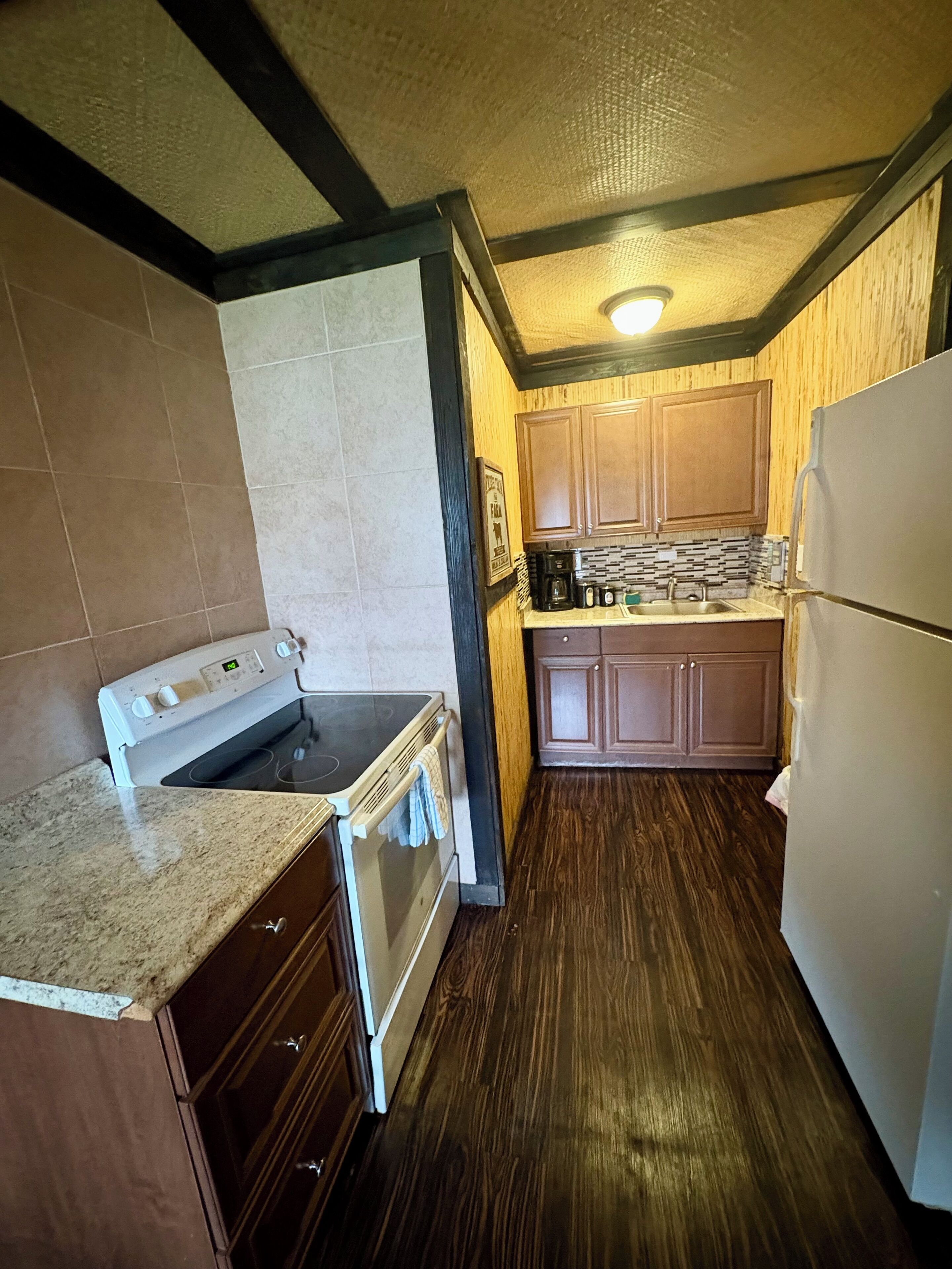 A compact kitchen with a stove, oven, sink, and wooden cabinets.
