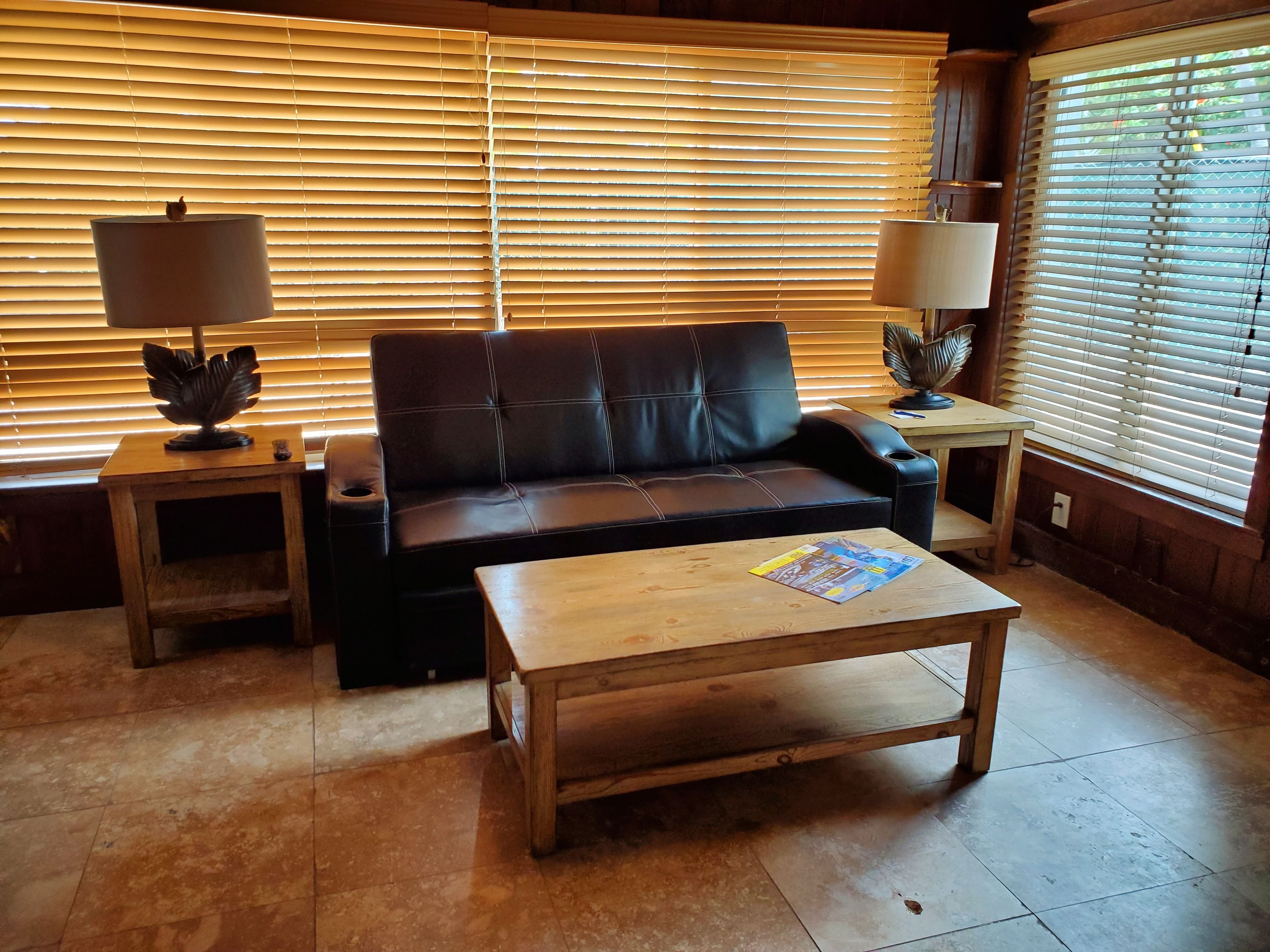 A living room with a sofa, two side tables, a coffee table, and a window with blinds.