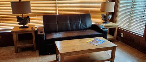 A living room with a sofa, two side tables, a coffee table, and a window with blinds.