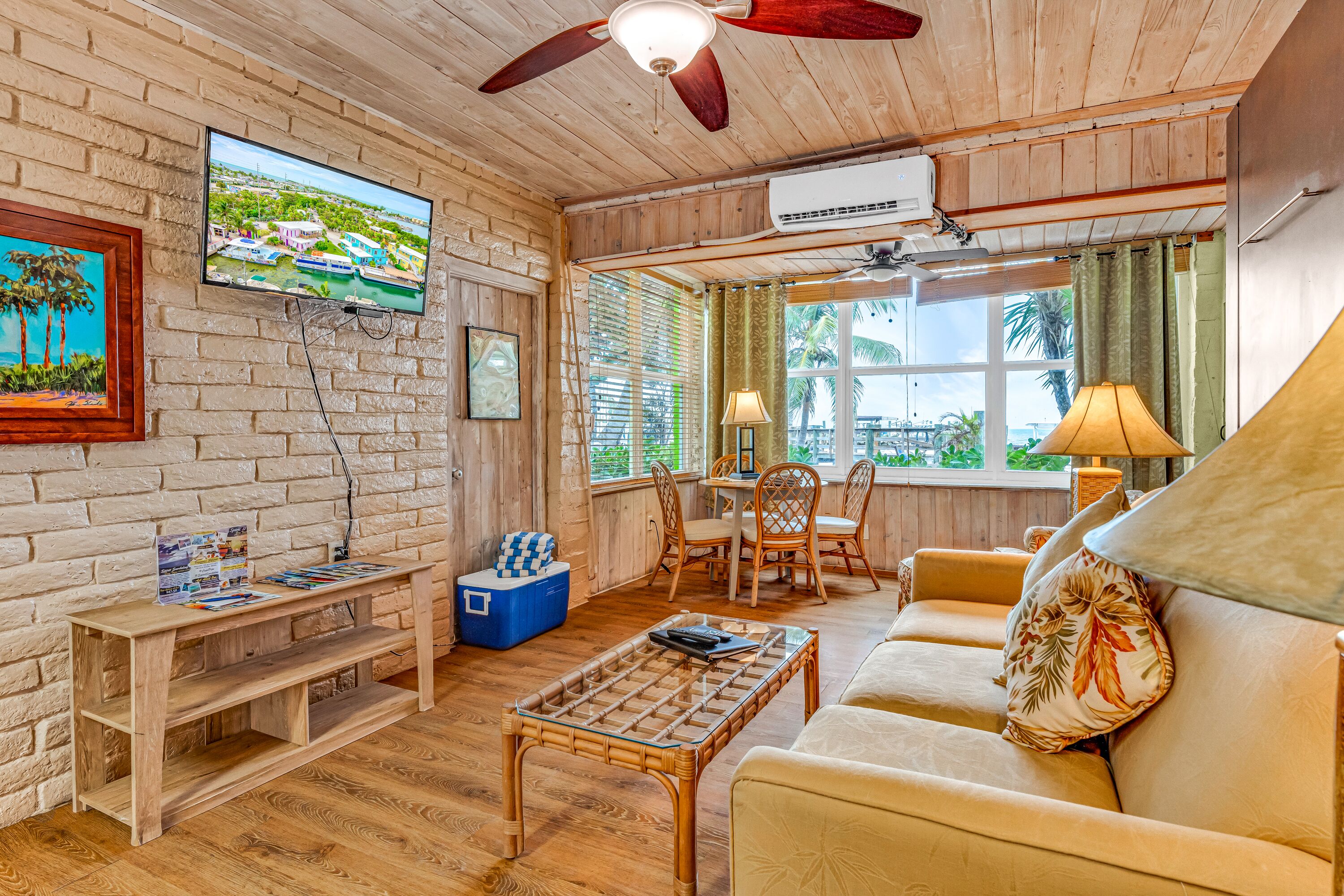 Una sala de estar con piso de madera, un televisor, un ventilador de techo, una mesa y un sofá.