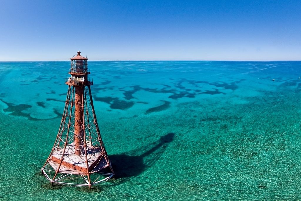 Un phare se dresse sur une mer bleue et limpide, entourée d’eaux cristallines.