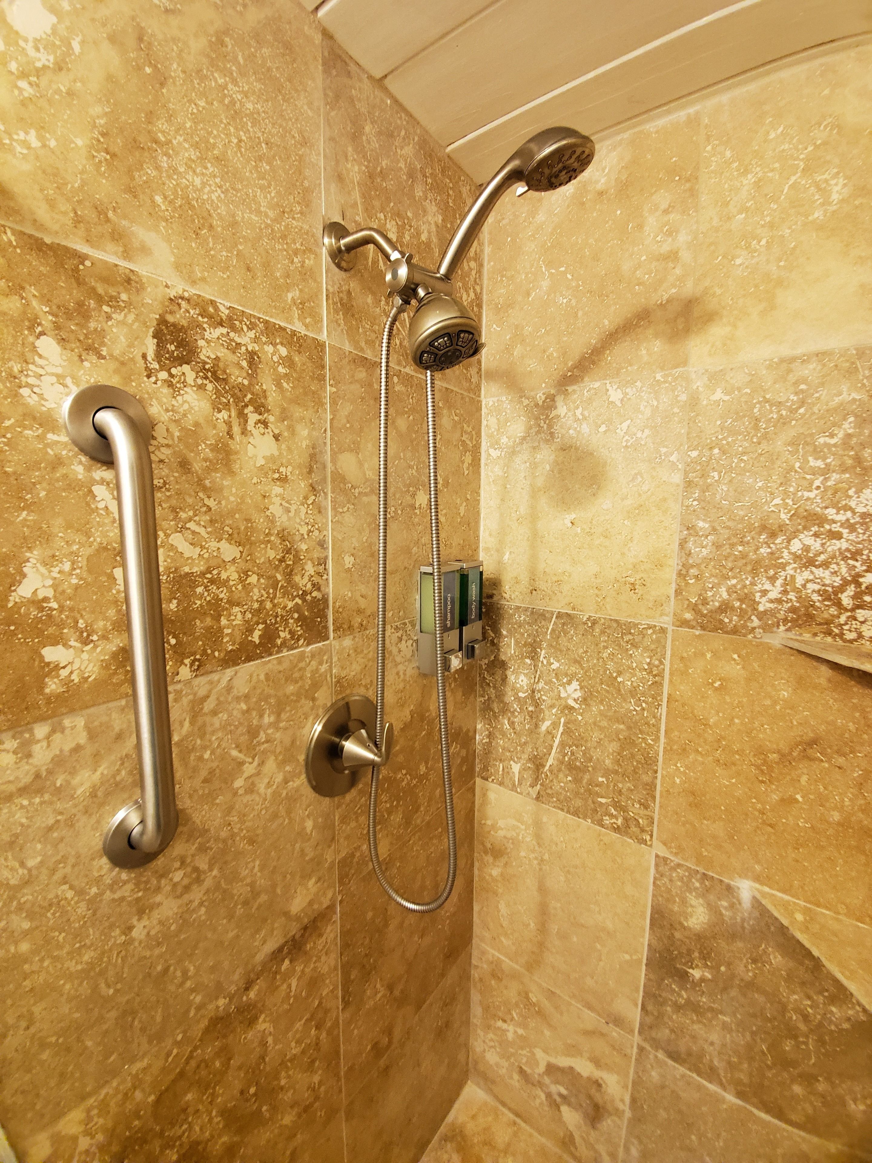 A shower with a handheld showerhead and a handheld shower attachment, mounted on a wall with a textured tile design.