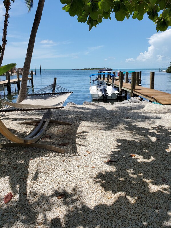 A hammock under a tree, a boat docked at a wooden pier, and a calm sea with a clear sky. - Captain Pips Marina & Hideaway (Marathon)