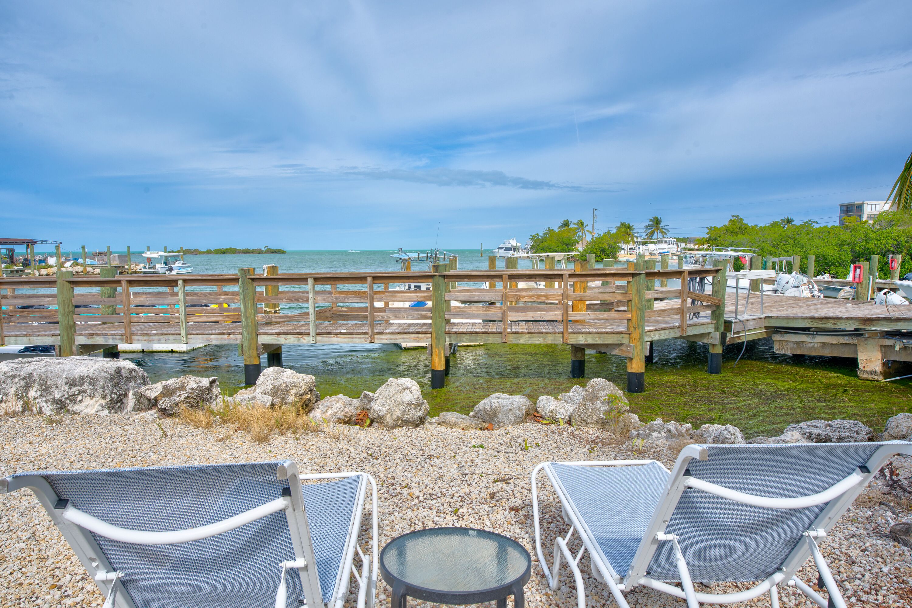 A waterfront patio with lounge chairs and a wooden dock extending into the water.