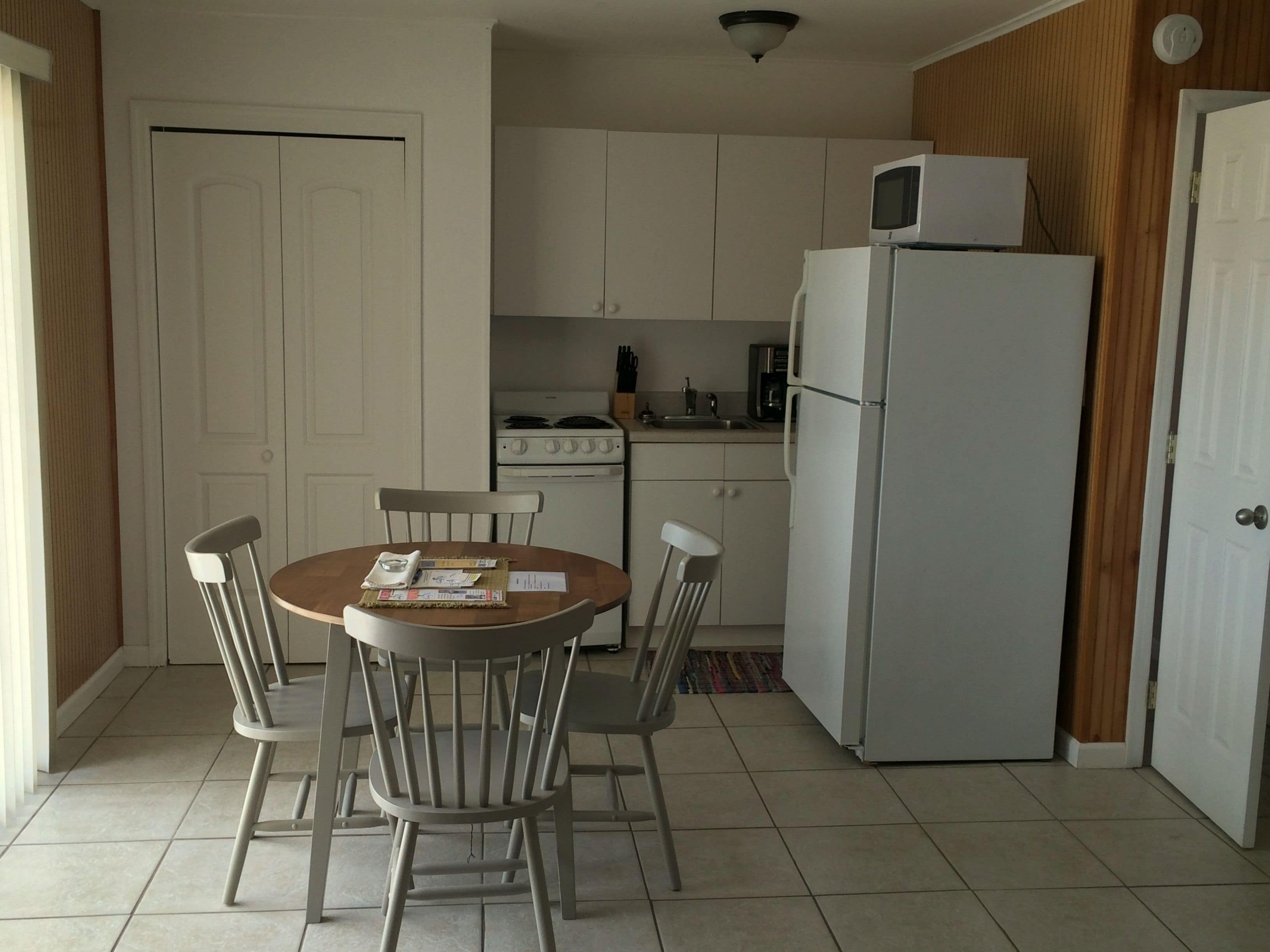 A compact kitchen with white cabinets, a stove, a microwave, and a refrigerator. There is a dining table with four chairs.