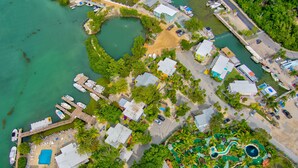 An aerial view of a coastal area with a marina, several boats, and a variety of buildings including a large resort with a pool and landscaped areas. - Captain Pips Marina & Hideaway (Marathon)