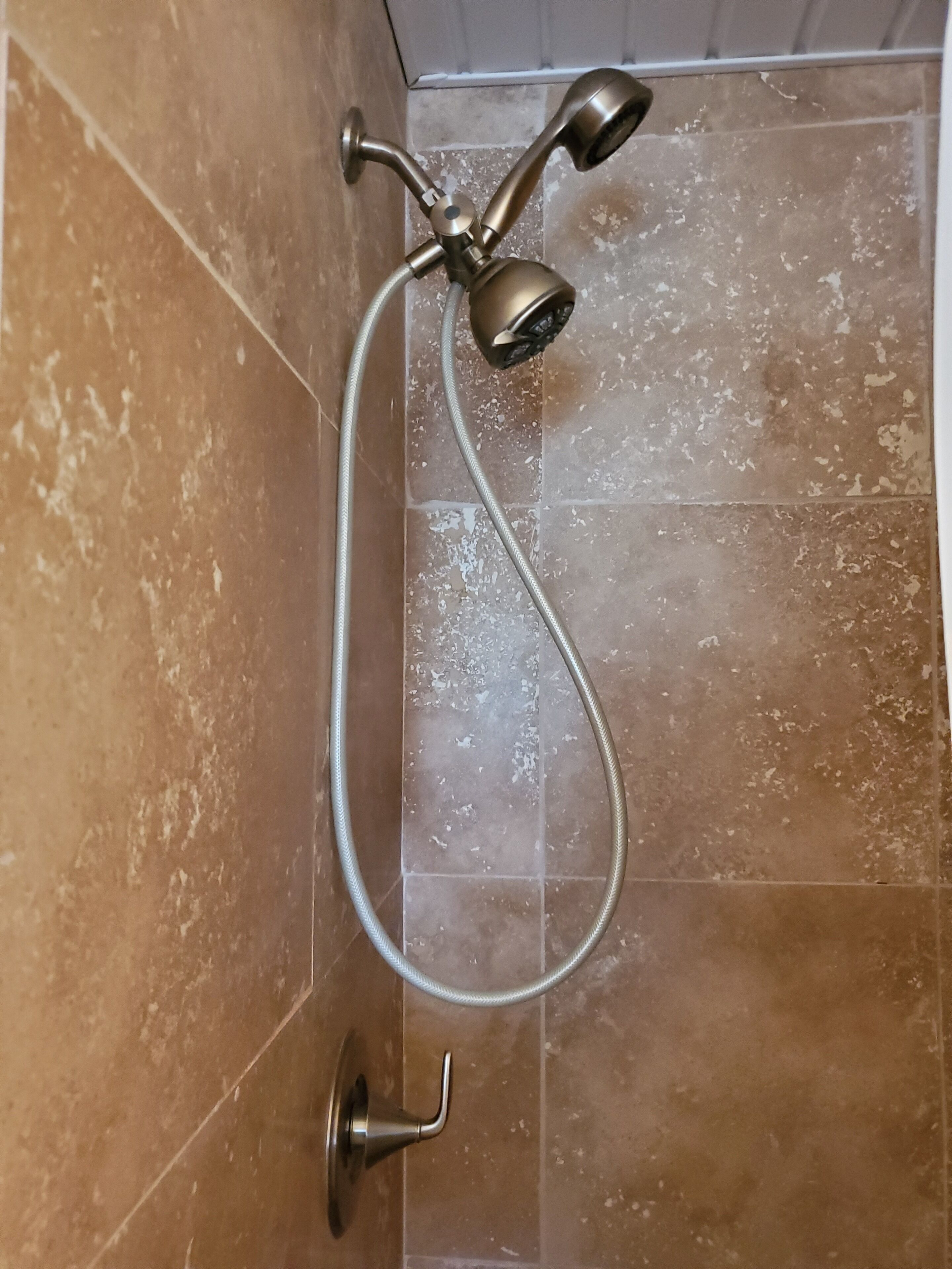A shower with a handheld showerhead and a wall-mounted faucet.