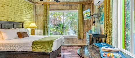 A room with a bed, a table with books, a ceiling fan, and a window with curtains.