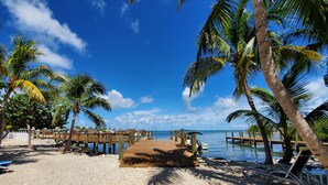 A beach with a wooden pier, palm trees, and a clear blue sky. - Captain Pips Marina & Hideaway (Marathon)