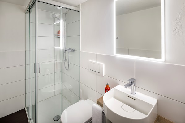 Un baño moderno con cabina de ducha de vidrio, un lavabo blanco y un espejo grande.