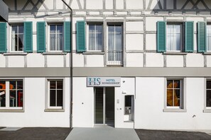 Hotel Schweizerhof features a traditional half-timbered facade with green shuttered windows and a glass door entrance.