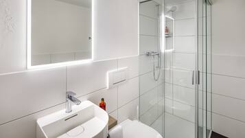 Une salle de bain moderne avec un lavabo blanc, des toilettes et une douche à parois de verre.