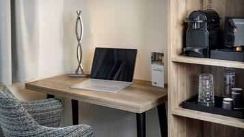 Um espaço de trabalho moderno com um laptop sobre uma mesa de madeira, uma máquina de café e um vaso de vidro em uma prateleira.