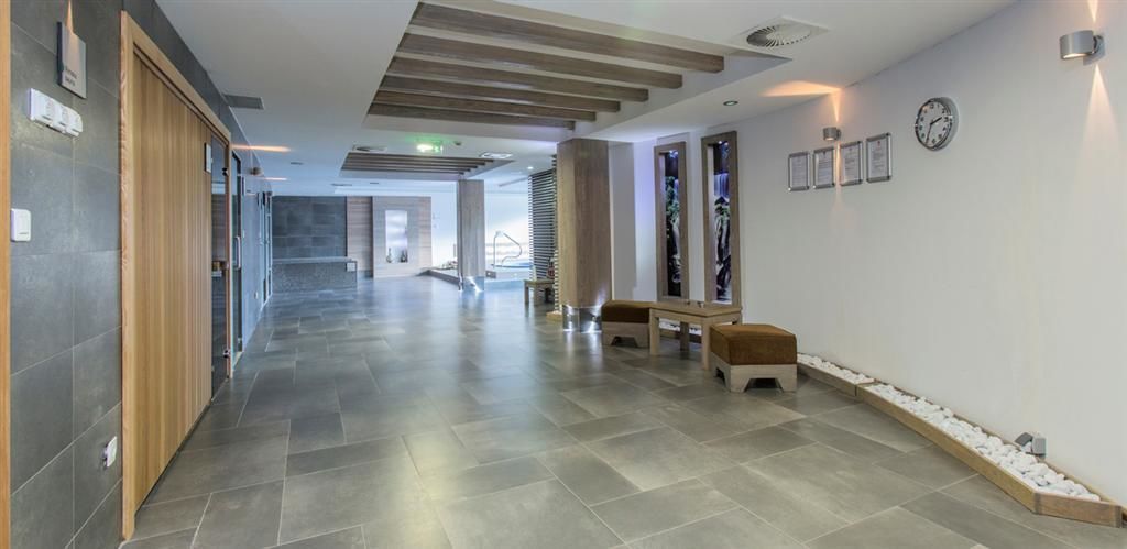 Un moderno vestíbulo de hotel con un largo pasillo, bancos, un mostrador de recepción y una escalera al fondo.