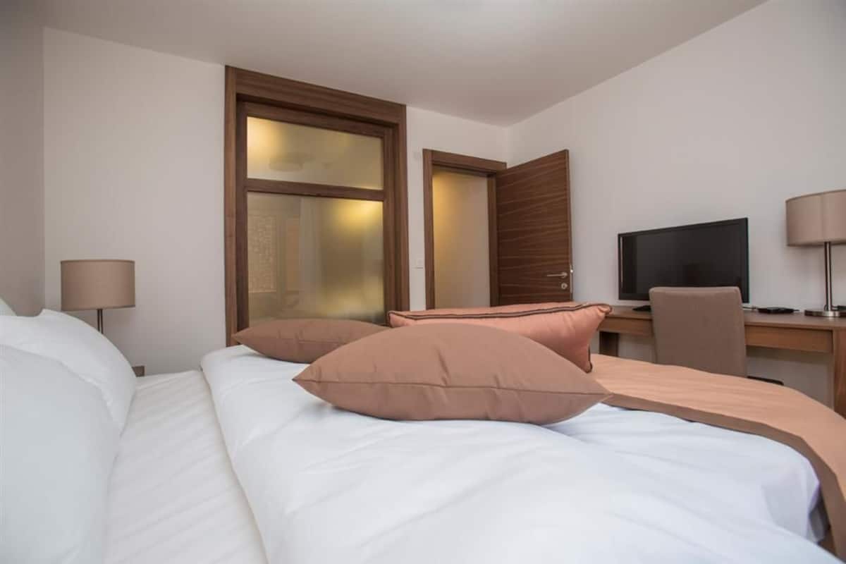 A hotel room with a bed, a desk, a television, and a door.