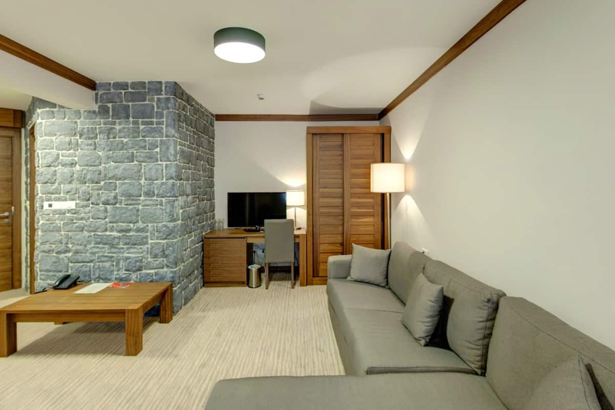 A modern living room with a stone accent wall, a wooden desk, a grey sofa, and a lamp.
