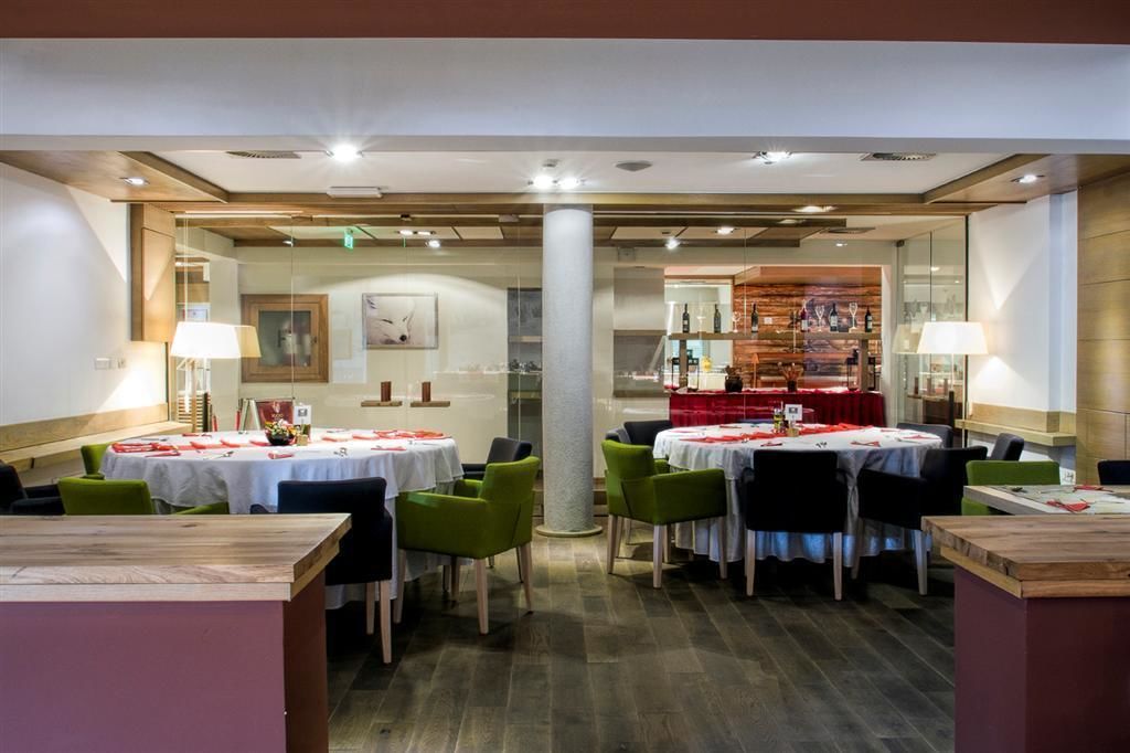 A restaurant with round tables, green chairs, and a red tablecloth.