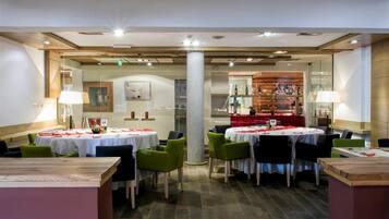A restaurant with round tables, green chairs, and a red tablecloth.