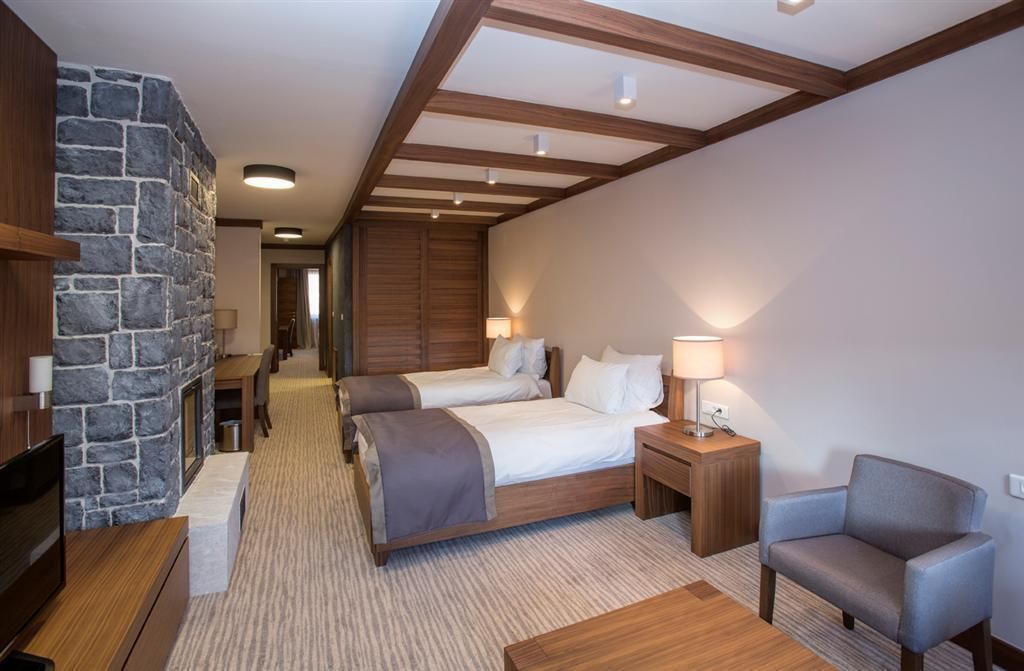 A hotel room with two beds, a stone accent wall, wooden beams, a television, a desk, and a chair.