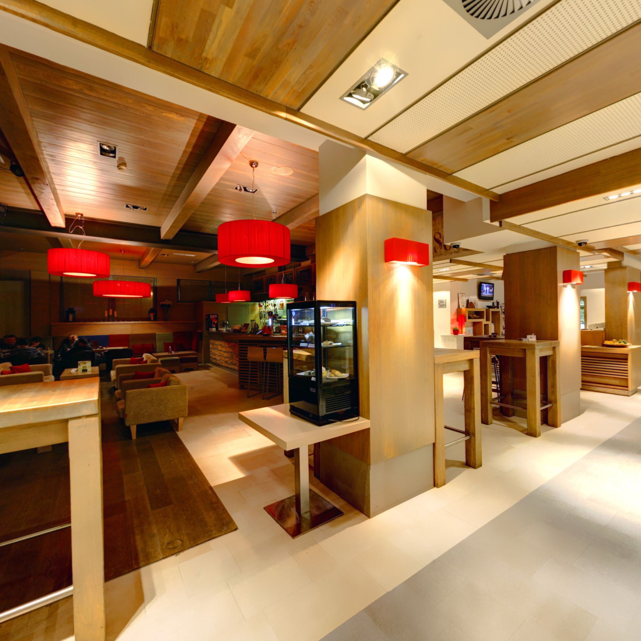 A modern interior with wooden beams, red pendant lights, and a bar area.