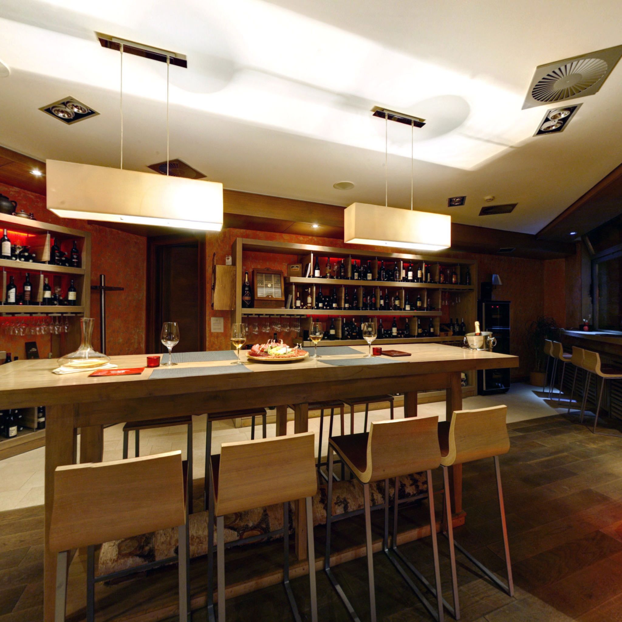 A bar area with a long counter, multiple wine bottles, and bar stools.