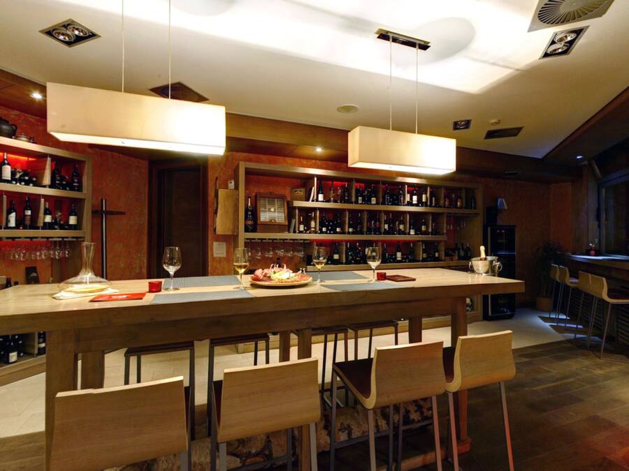A bar area with a long counter, multiple wine bottles, and bar stools.