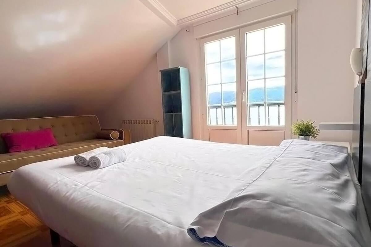 Ein Schlafzimmer mit einem großen Bett, einem Fenster mit Blick, einer Couch und einer Pflanze.