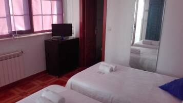 A hotel room with two beds, a TV on a stand, a mirror, and a window with blinds.