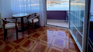 Un balcon donnant sur un plan d’eau et des bâtiments, une table ronde avec des chaises, et une porte-fenêtre coulissante.
