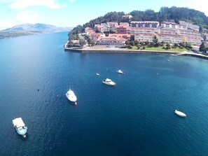 Une vue aérienne d’une ville côtière, avec plusieurs bateaux sur l’eau et un ensemble de bâtiments aux toits rouges.